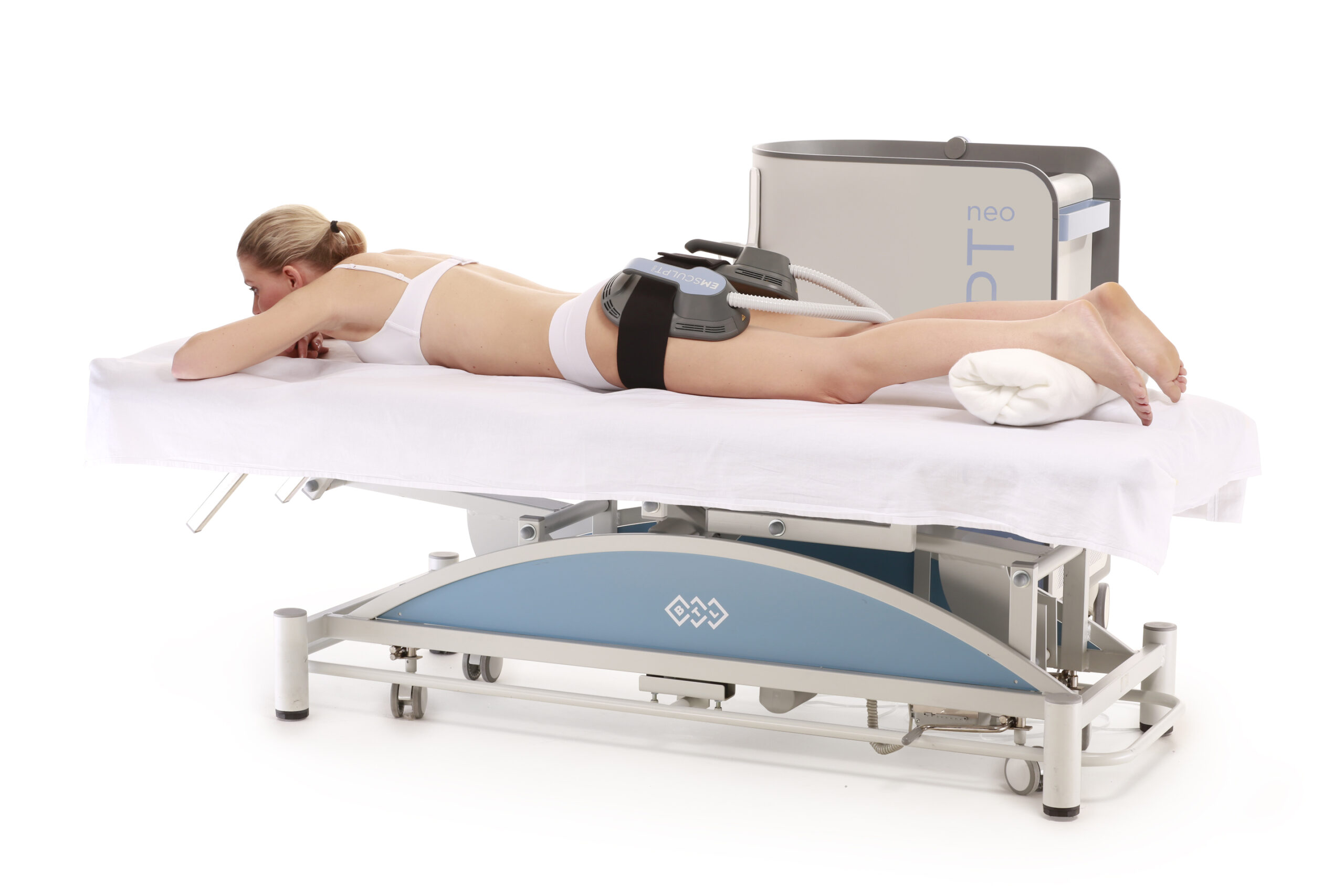 woman laying on a platform with blankets receiving treatment from the emsculpt neo machine